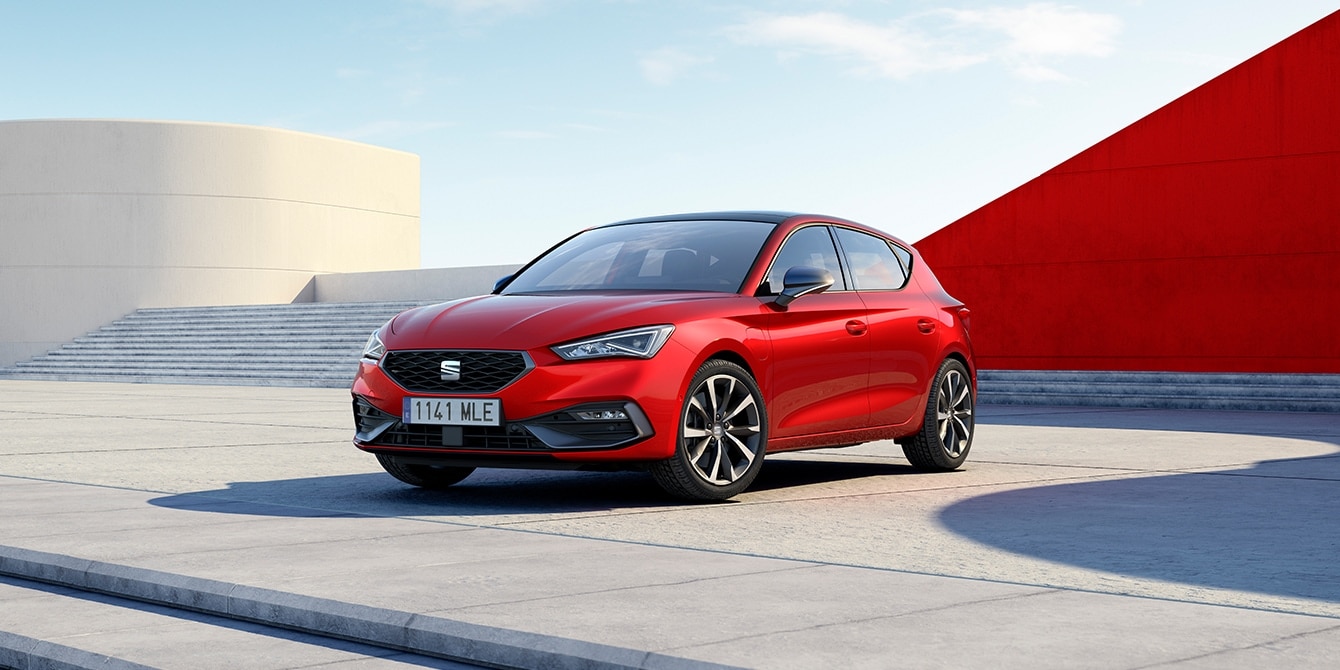 SEAT Leon 5D in Desire Red parked in a minimalist urban square under a clear blue sky, with modern geometric architecture.