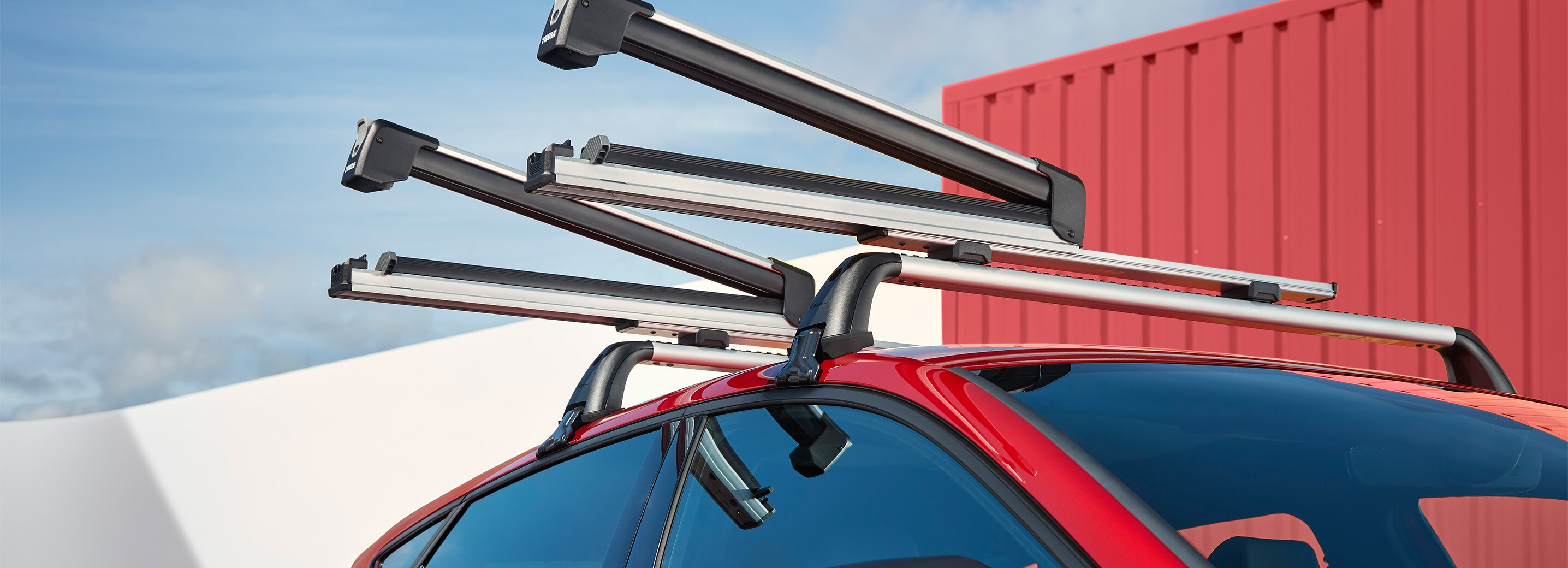 A red SEAT Leon parked in an outdoors environment, showcasing the roof rack that secures several skis.