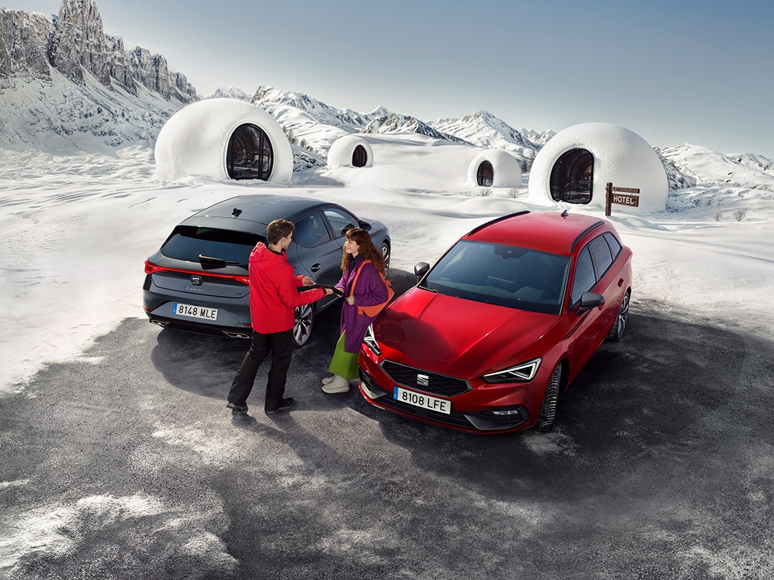 A person loading skis onto a SEAT Leon 5D equipped with a roof-mounted Ski Rack Xtender in a snowy setting.