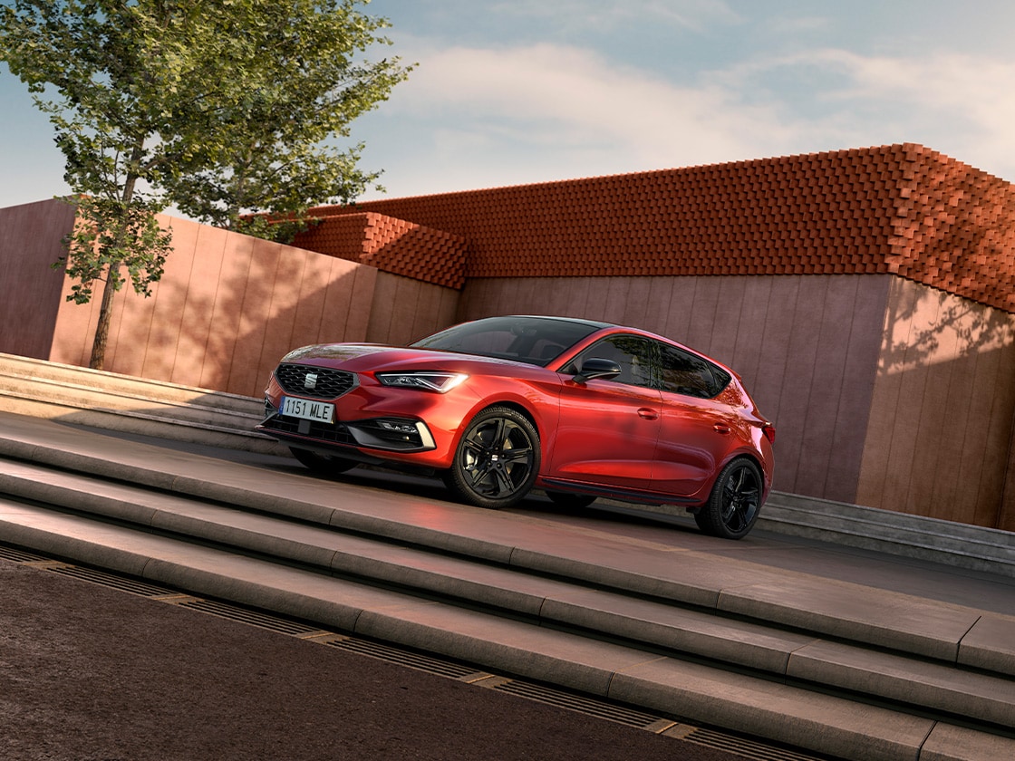 Glossy black mirror covers for the SEAT Leon FR contrasting with the red car body, side view with cement background.