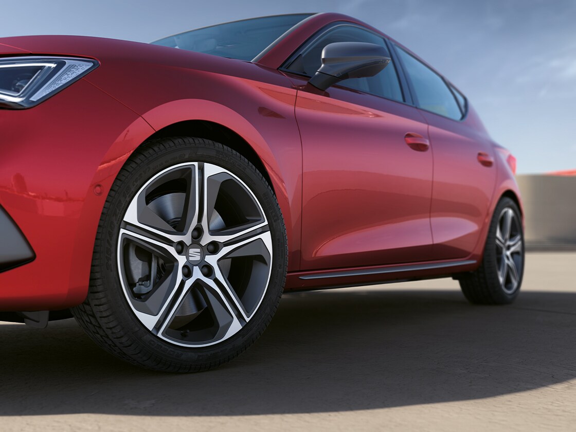 A desire red SEAT Leon focusing on the side door moulding and alloy wheel, with the car parked under a clear sky.