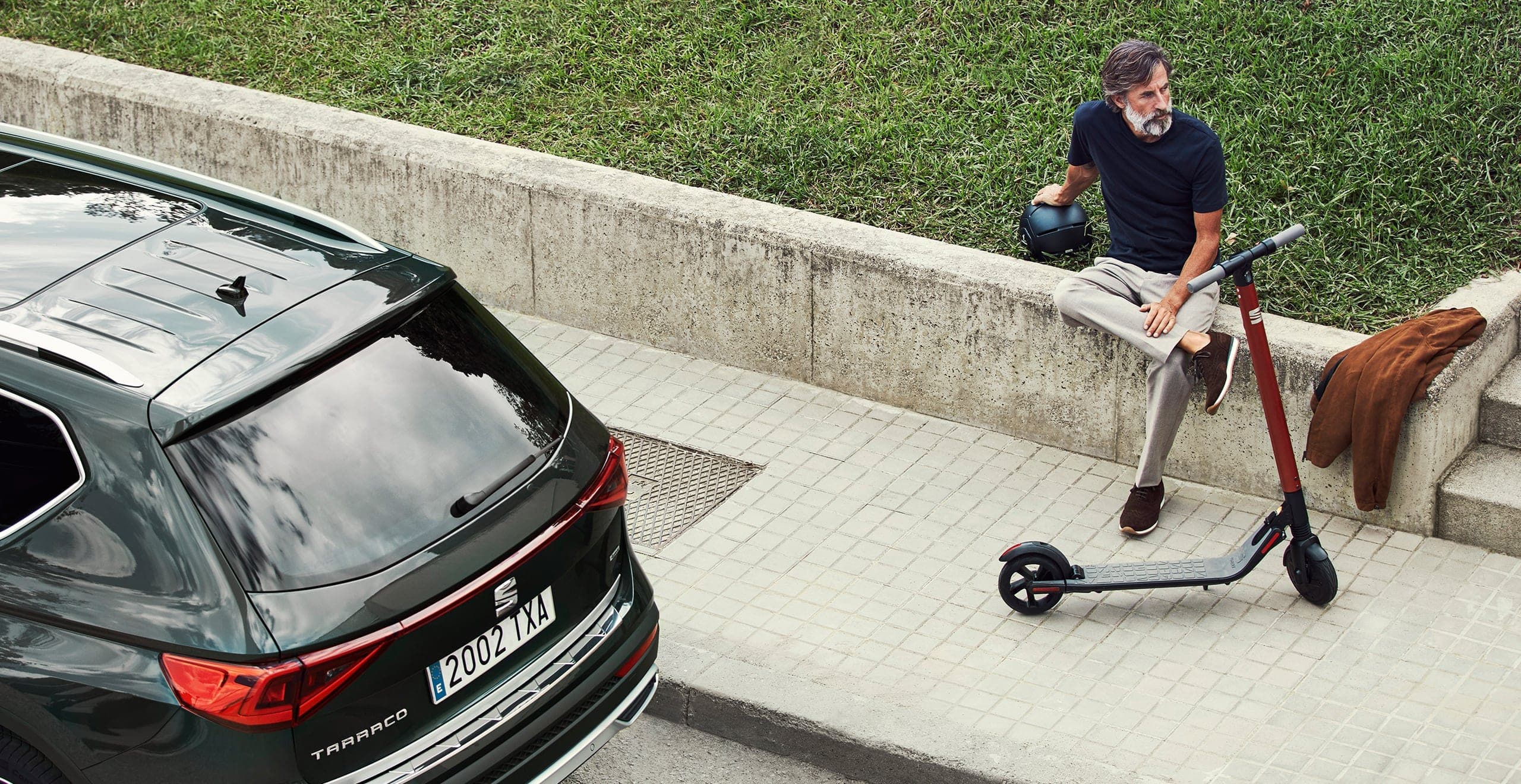 SEAT eXS KickScooter urban mobility solution powered by Segway - Man walking next to Tarraco large SUV