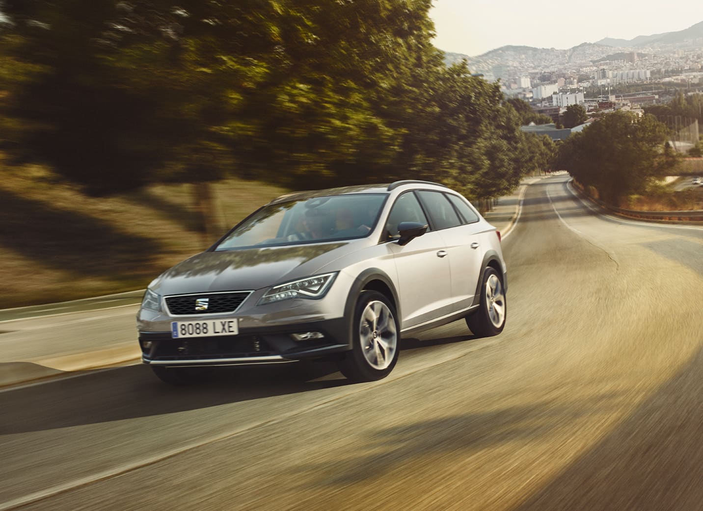 SEAT Leon car driving on an empty road surrounded by fields and trees