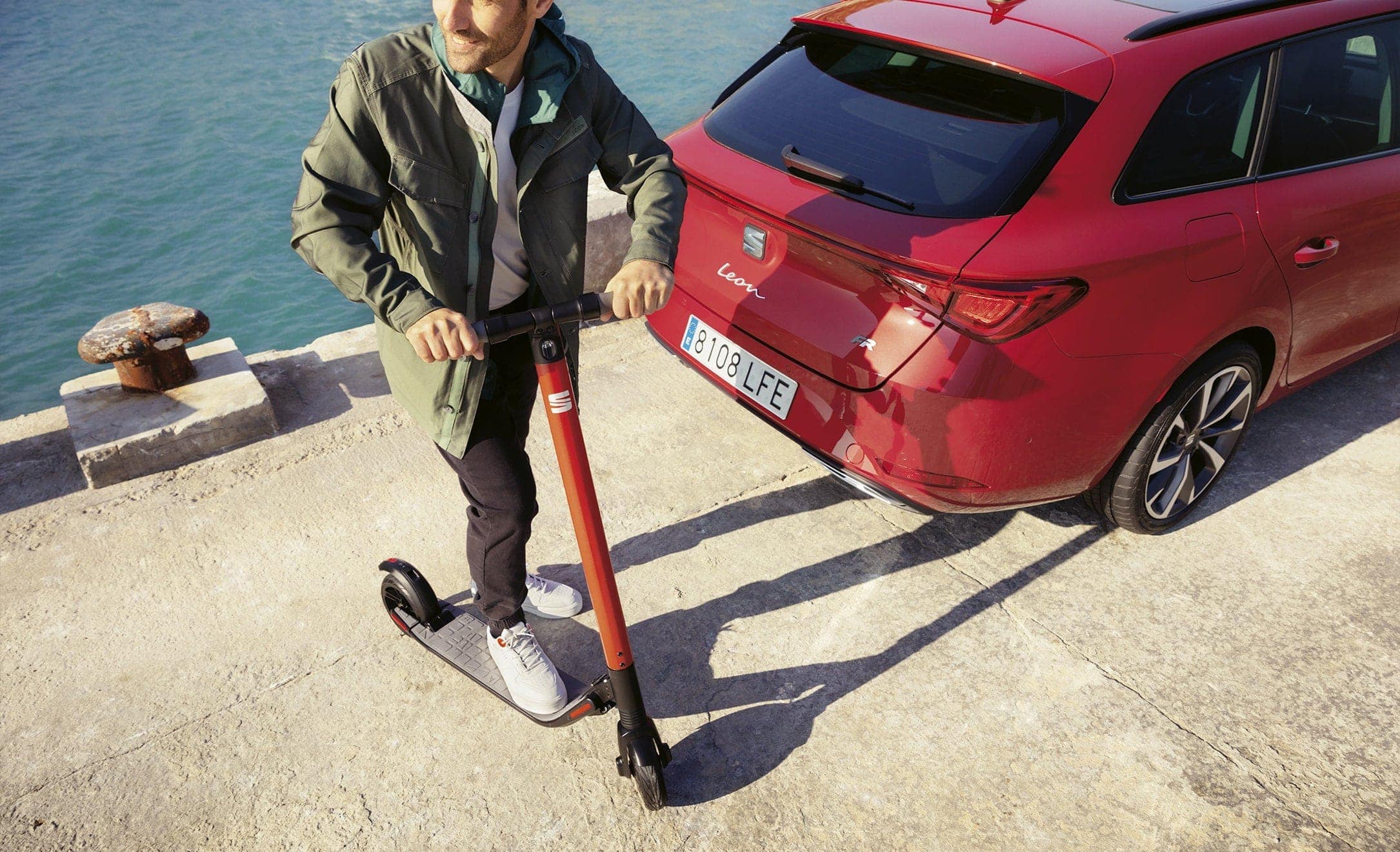 SEAT EXS KickScooter urban mobility solution powered by Segway man walking next to SEAT Leon Sportstourer